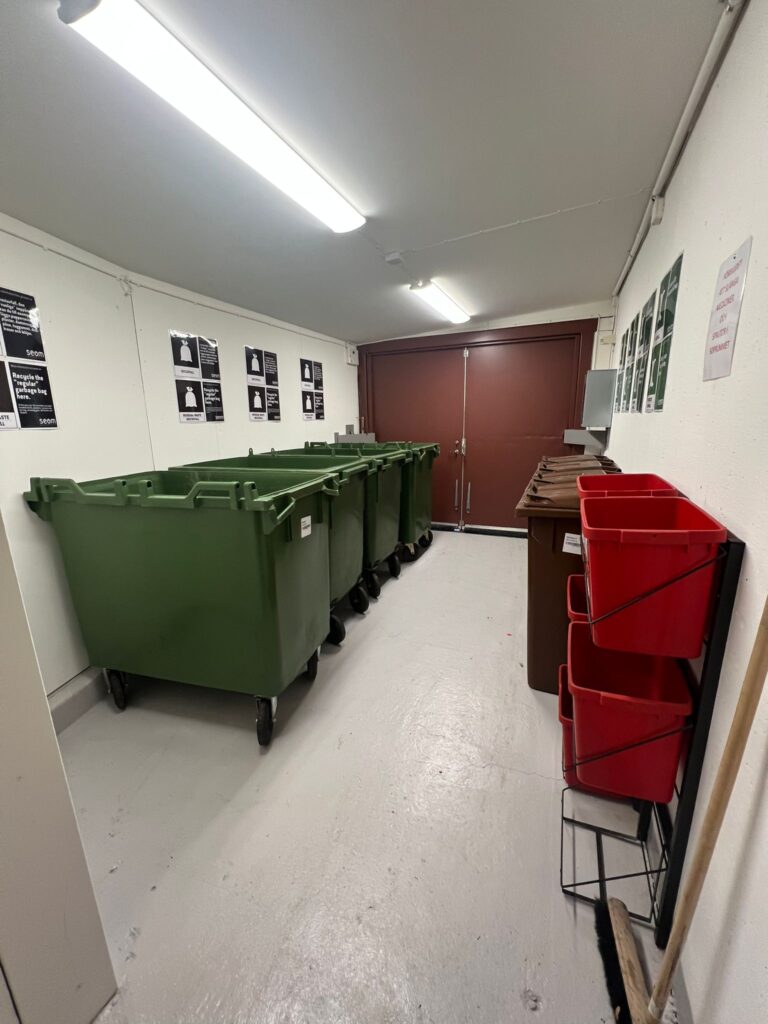 Bild på fyra gröna sopkärl i nya utrymmet i soprum z6. Till höger om bilden syns kärl för matavfall.